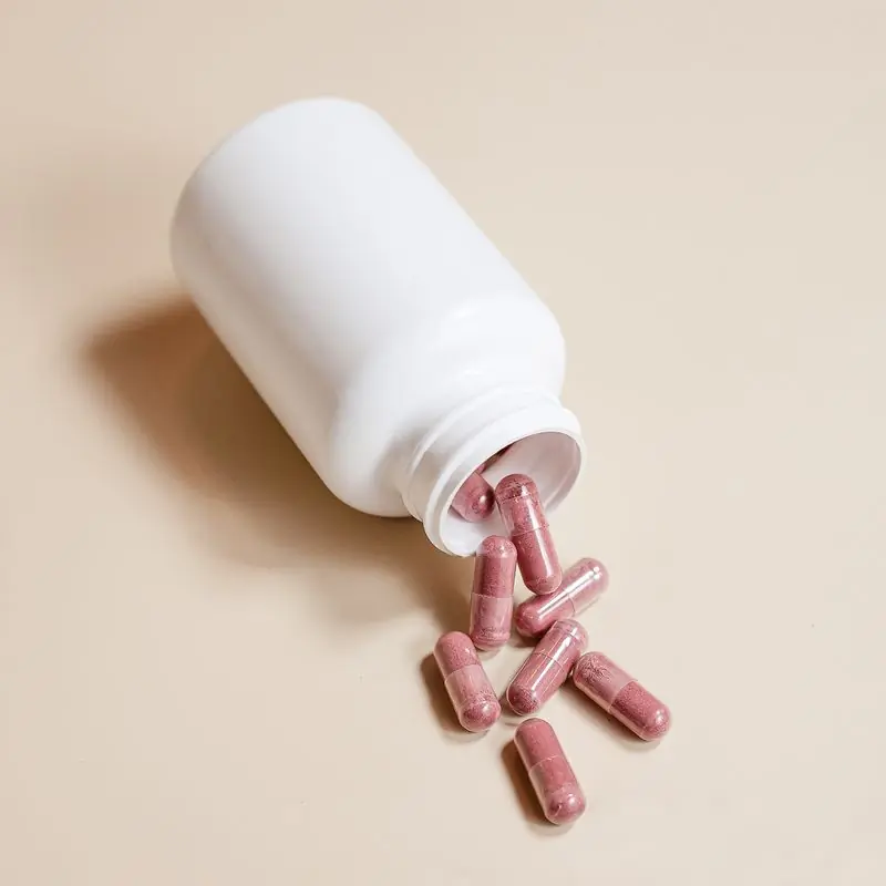 A white bottle on its side with capsules spilling out across a beige surface