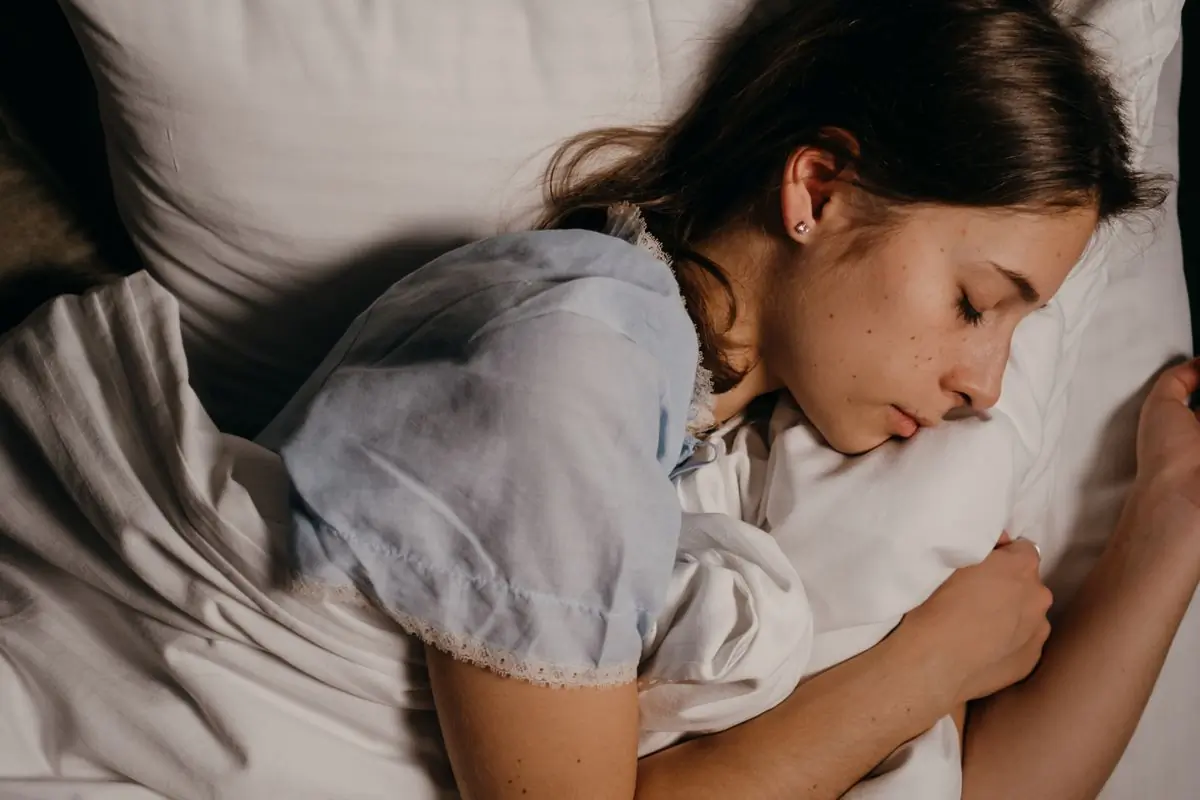 A young woman asleep on a white pillow under soft, low evening light