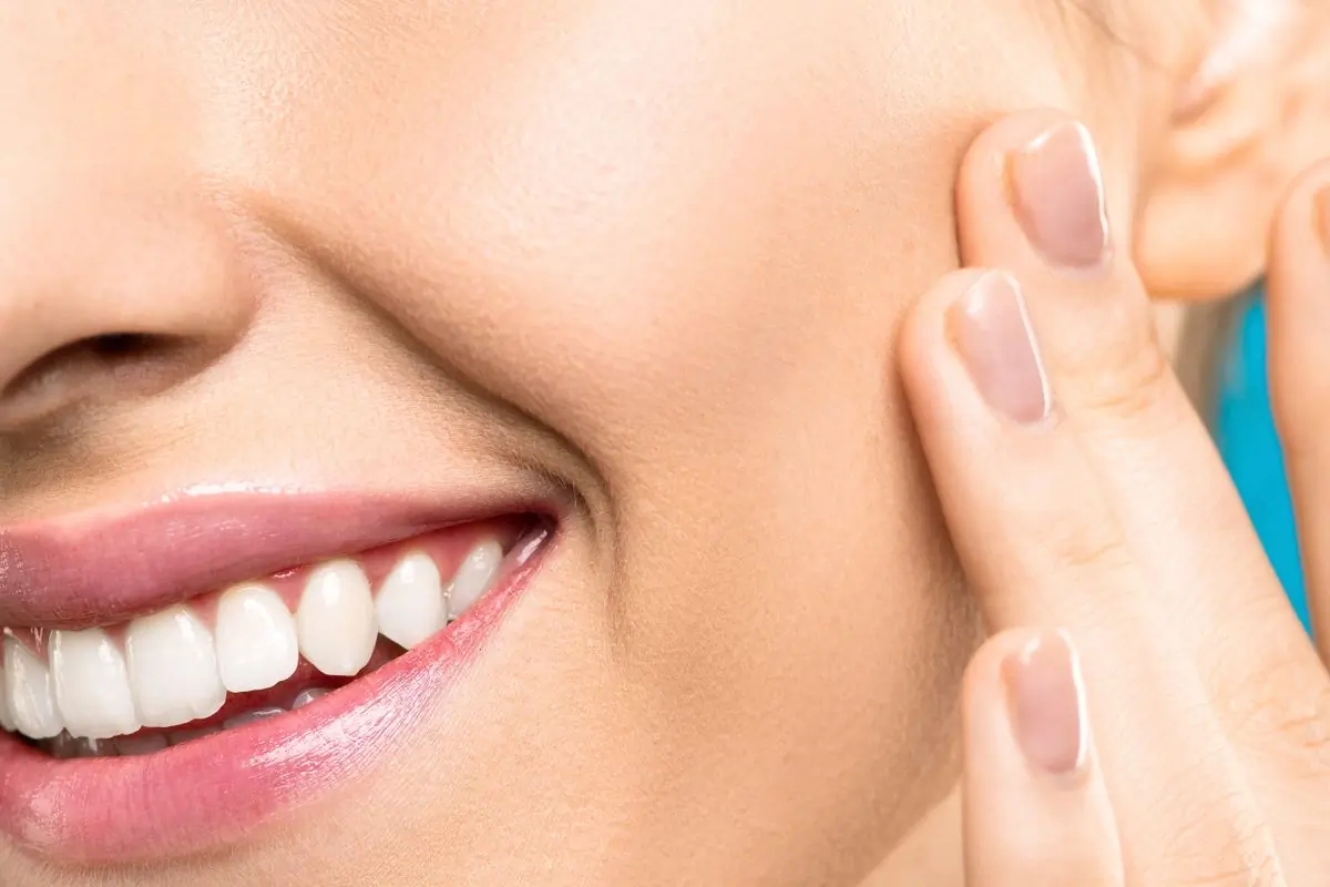 A smiling woman touching her cheek in close-up, showing clear, healthy skin