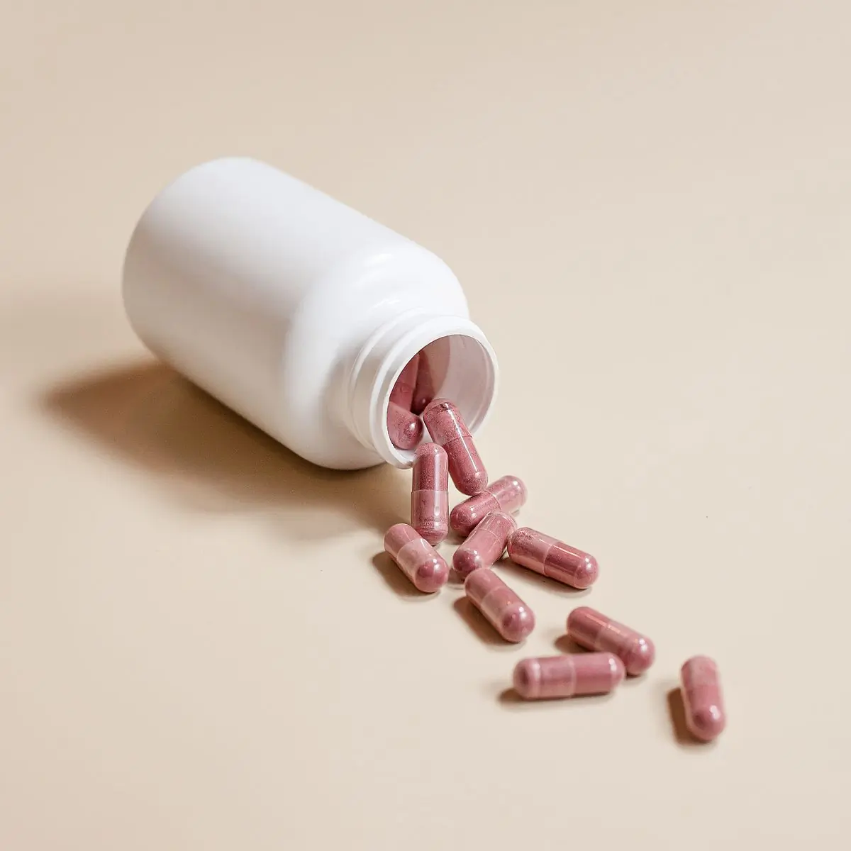 The bottle tipped over, spilling a scatter of capsules across a warm beige surface