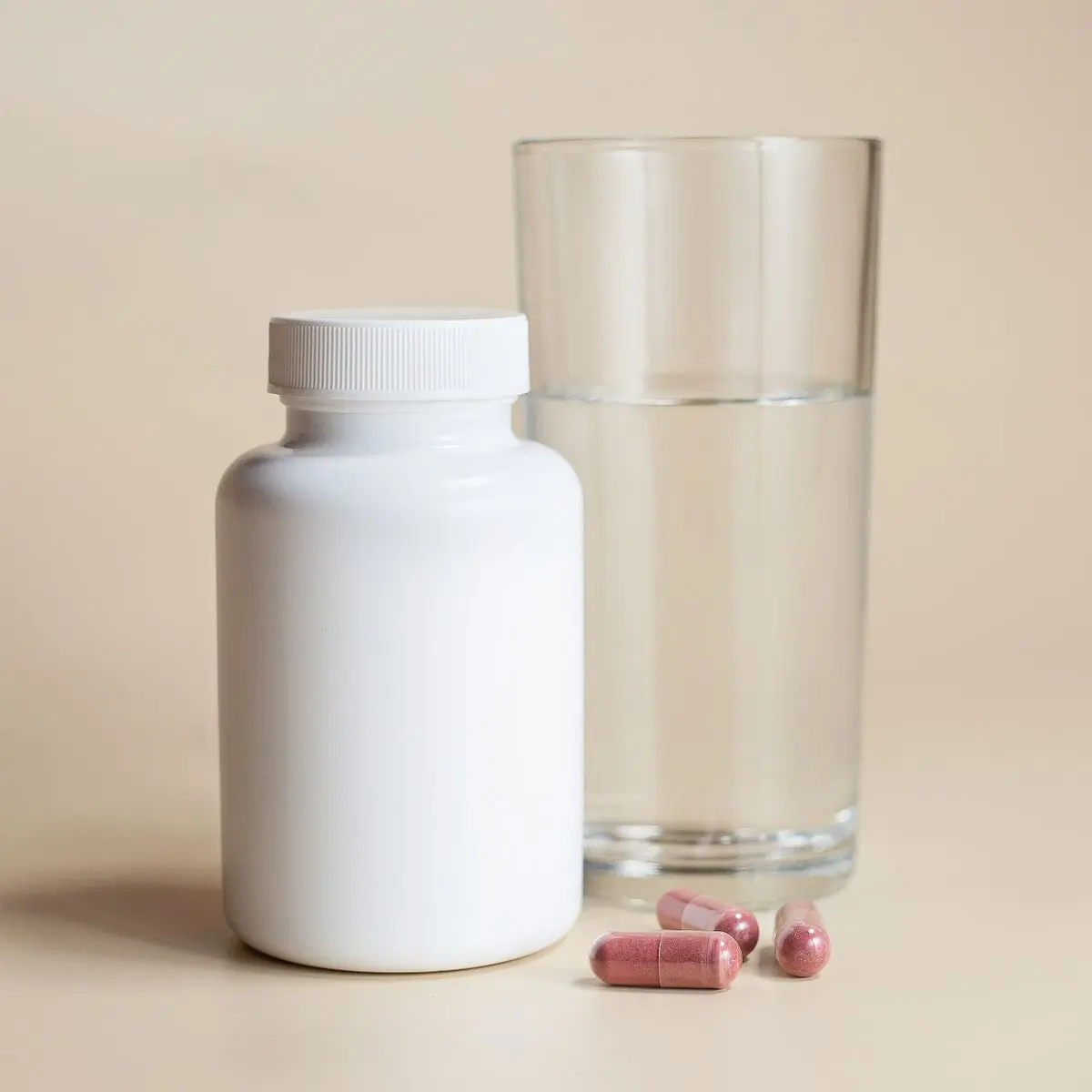 The bottle beside a tall glass of water with capsules in front of it on beige