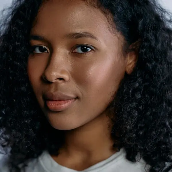 A head-and-shoulders portrait of a woman with natural curly hair against a plain pale backdrop