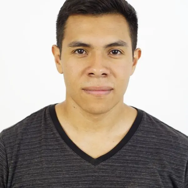 A head-and-shoulders portrait of a man in a grey v-neck t-shirt against a white background
