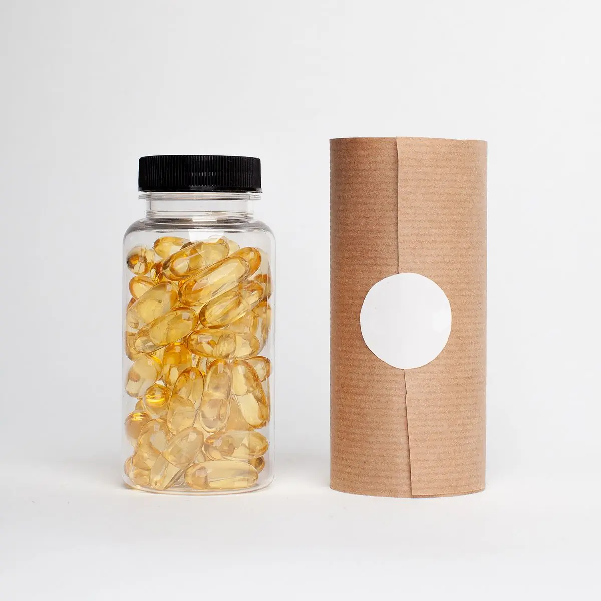 A clear jar packed with golden softgel capsules standing beside a kraft paper tube