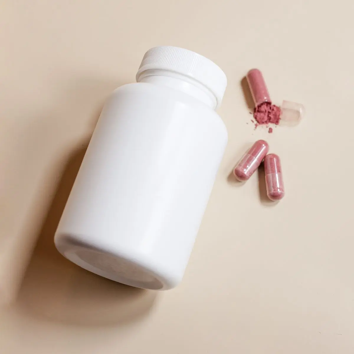 A white supplement bottle seen from above beside capsules, one opened to show its powder