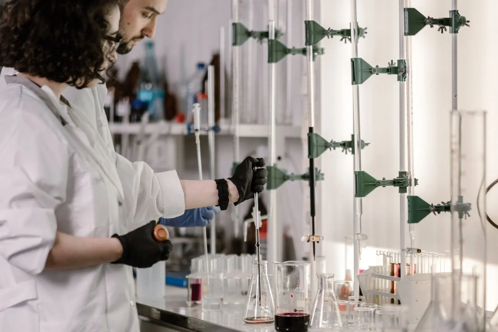 Two scientists in white coats working with pipettes and glassware at a laboratory bench