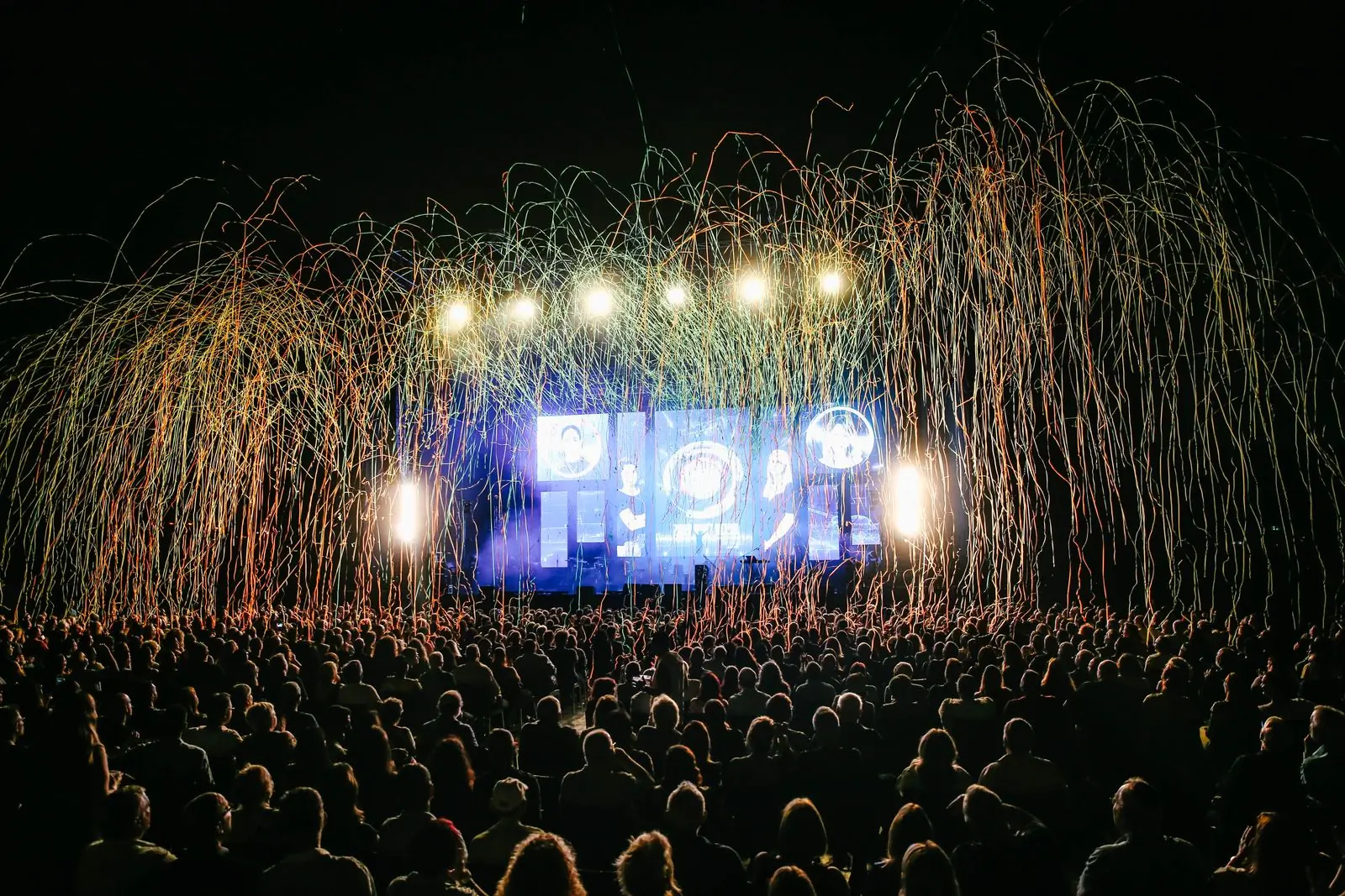 A festival crowd in front of a lit main stage at night