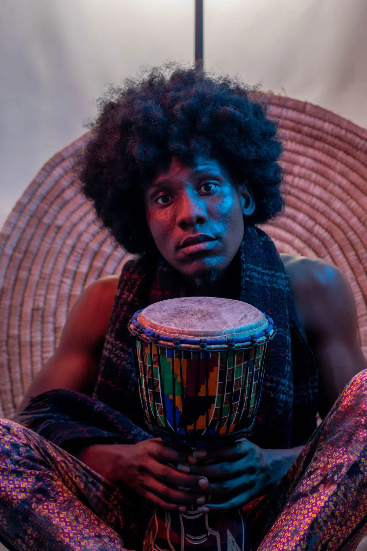 A drummer photographed under blue stage light with a hand drum between his knees
