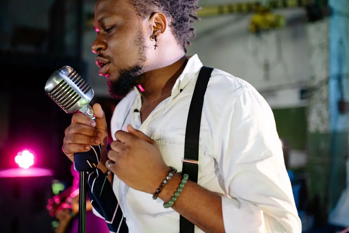 A man singing into a vintage microphone under warm stage light