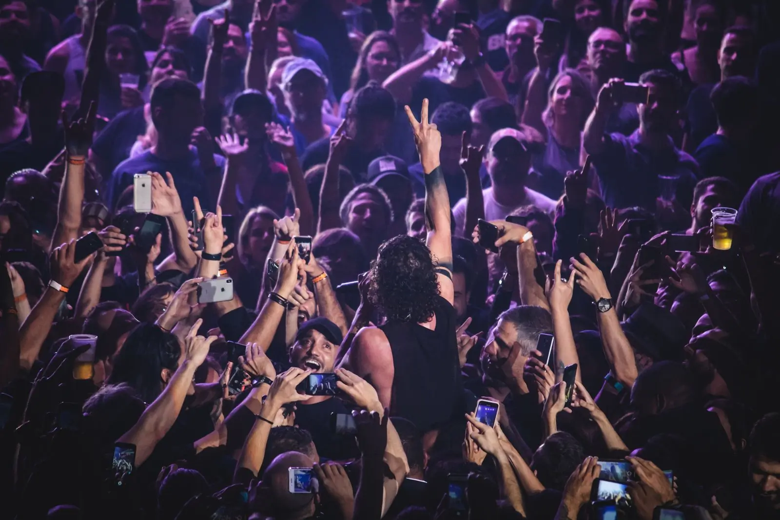 A dense festival crowd with phones and hands held above their heads