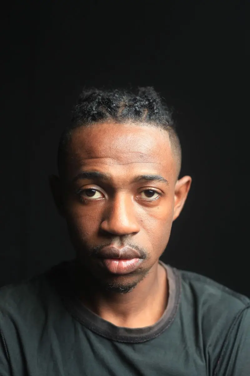 A man with braided hair photographed against a dark studio ground