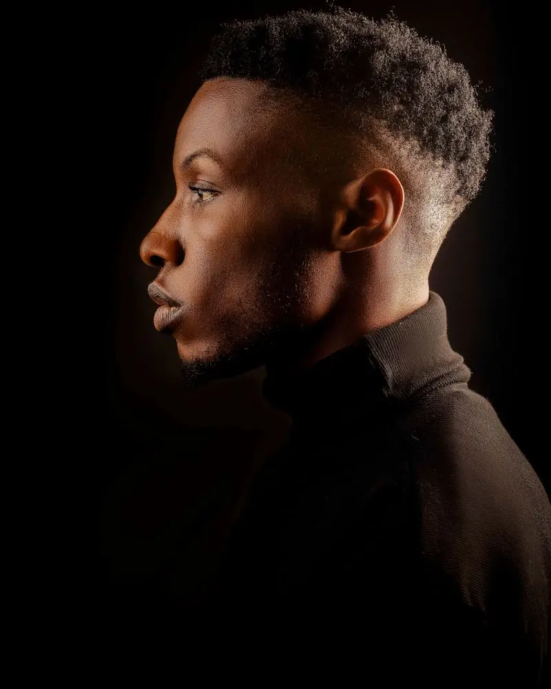 A man photographed in profile against a black studio ground
