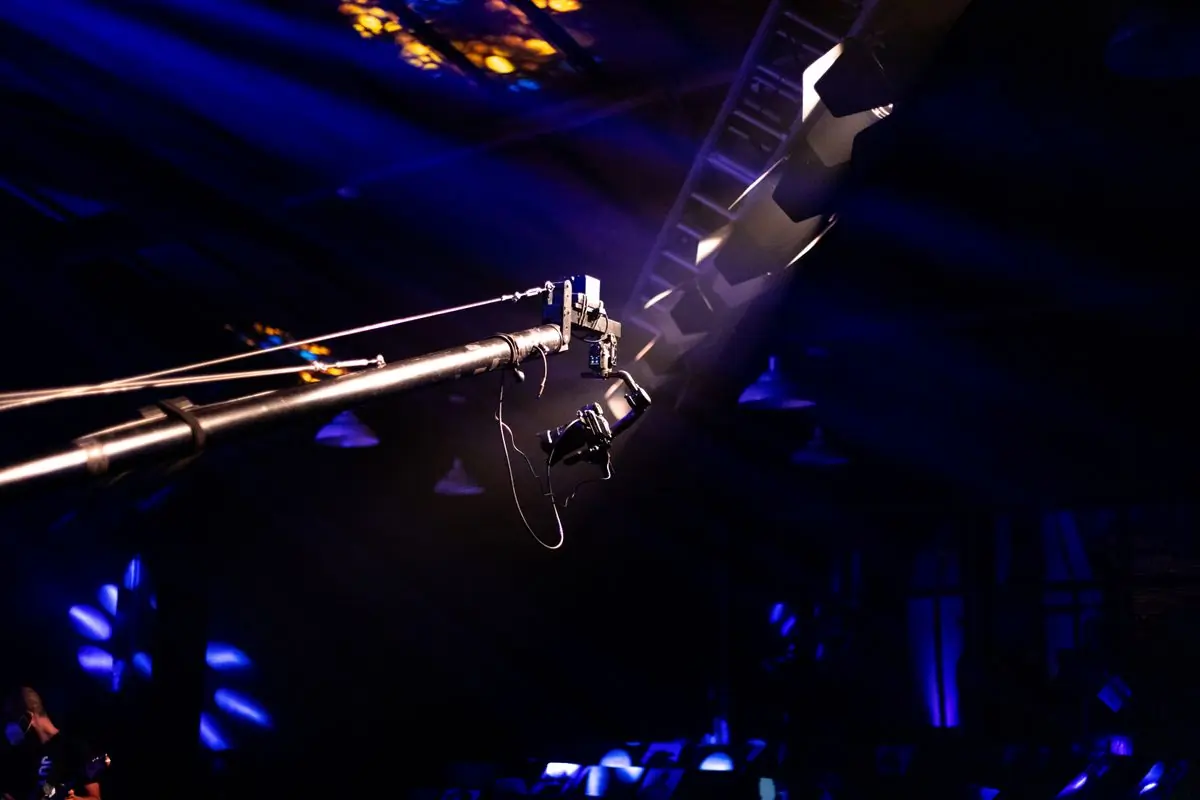 A camera crane set up at a concert venue under coloured light