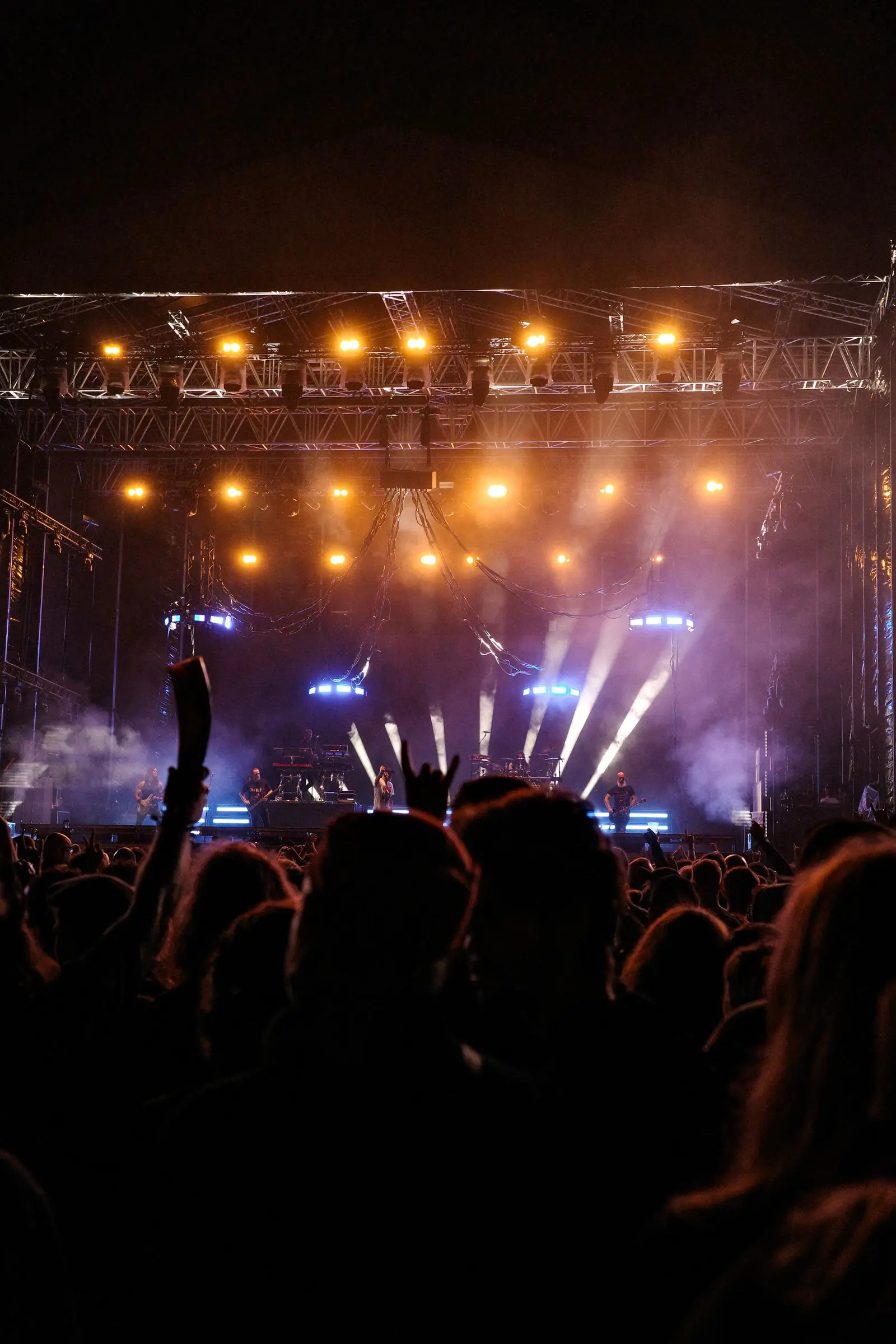 A crowd with raised hands under orange stage lights