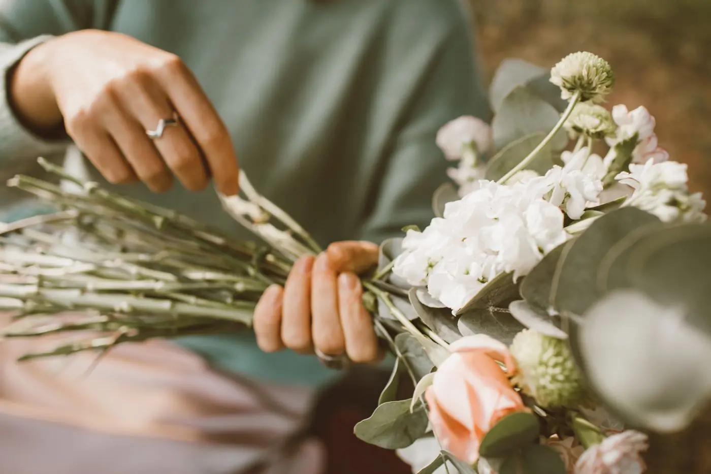 Hands binding a bouquet of pale flowers and eucalyptus