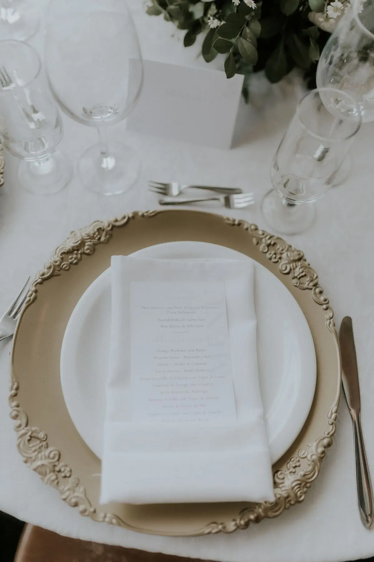 A gold-rimmed charger plate set with a folded napkin and a printed menu card