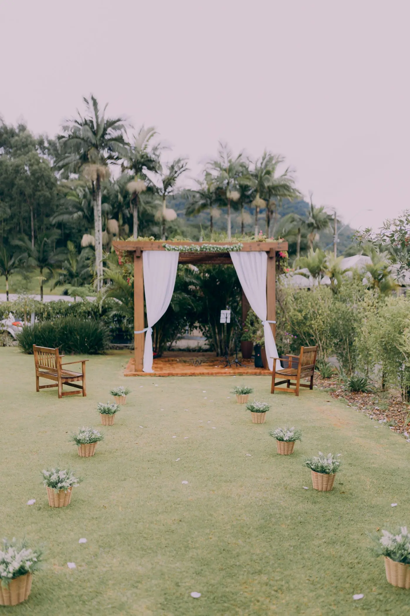 A draped garden canopy with two chairs set for a ceremony under palms