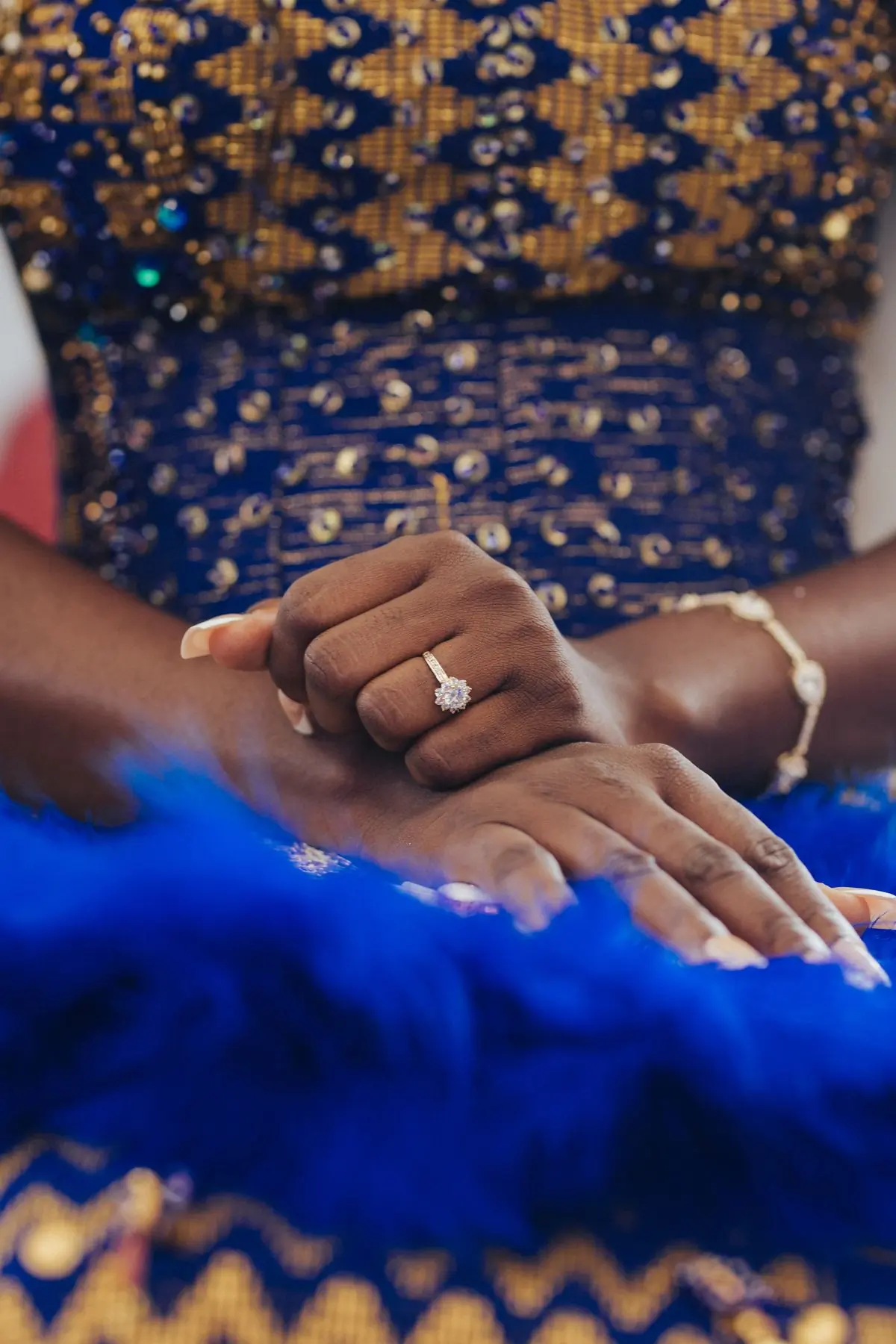 A bride's hands resting together, an engagement ring against blue lace