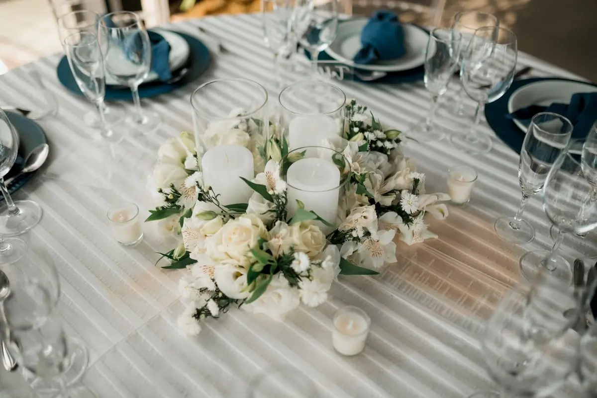 A low arrangement of white flowers and candles down a dressed table