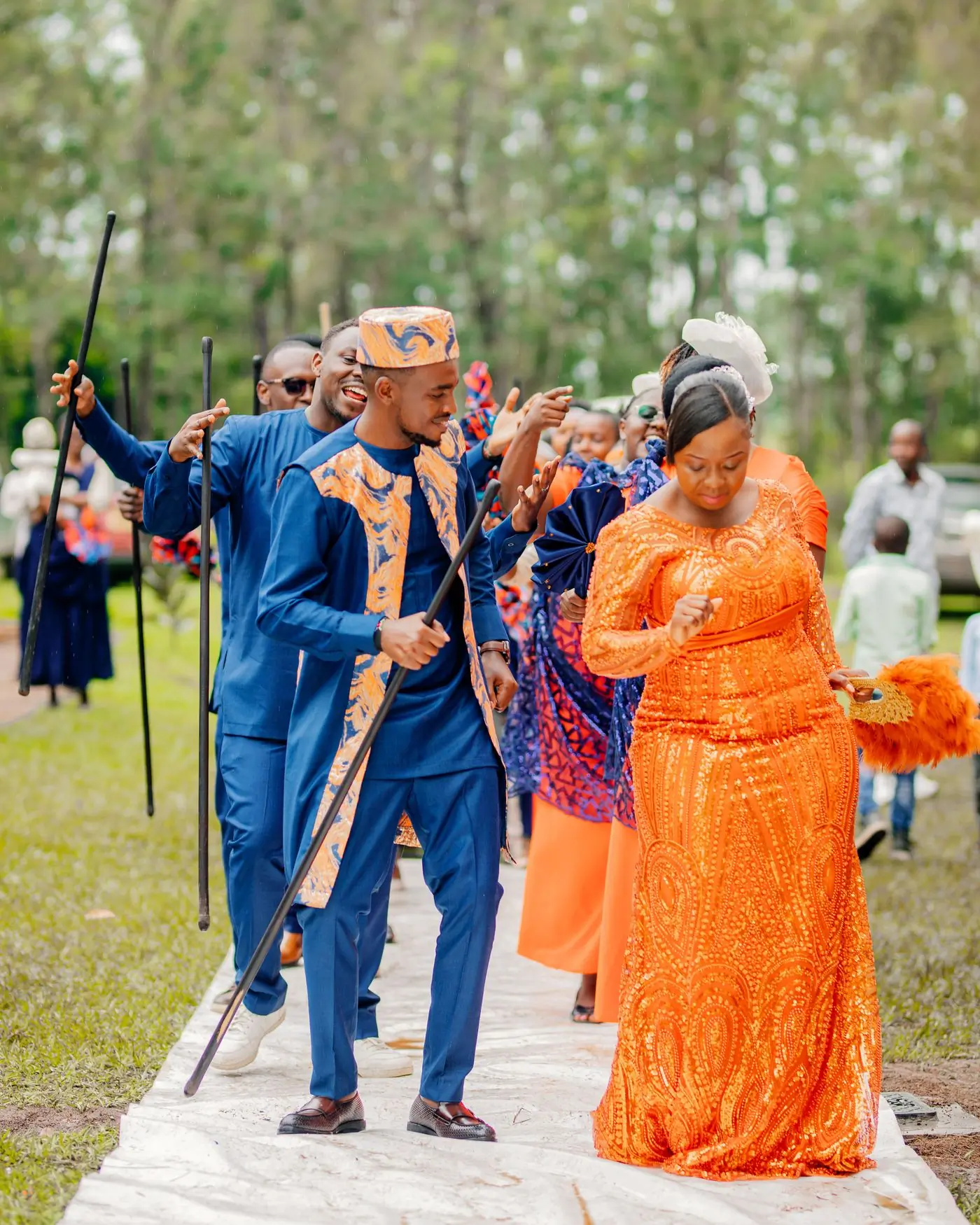 A wedding procession in blue and orange traditional dress crossing a lawn
