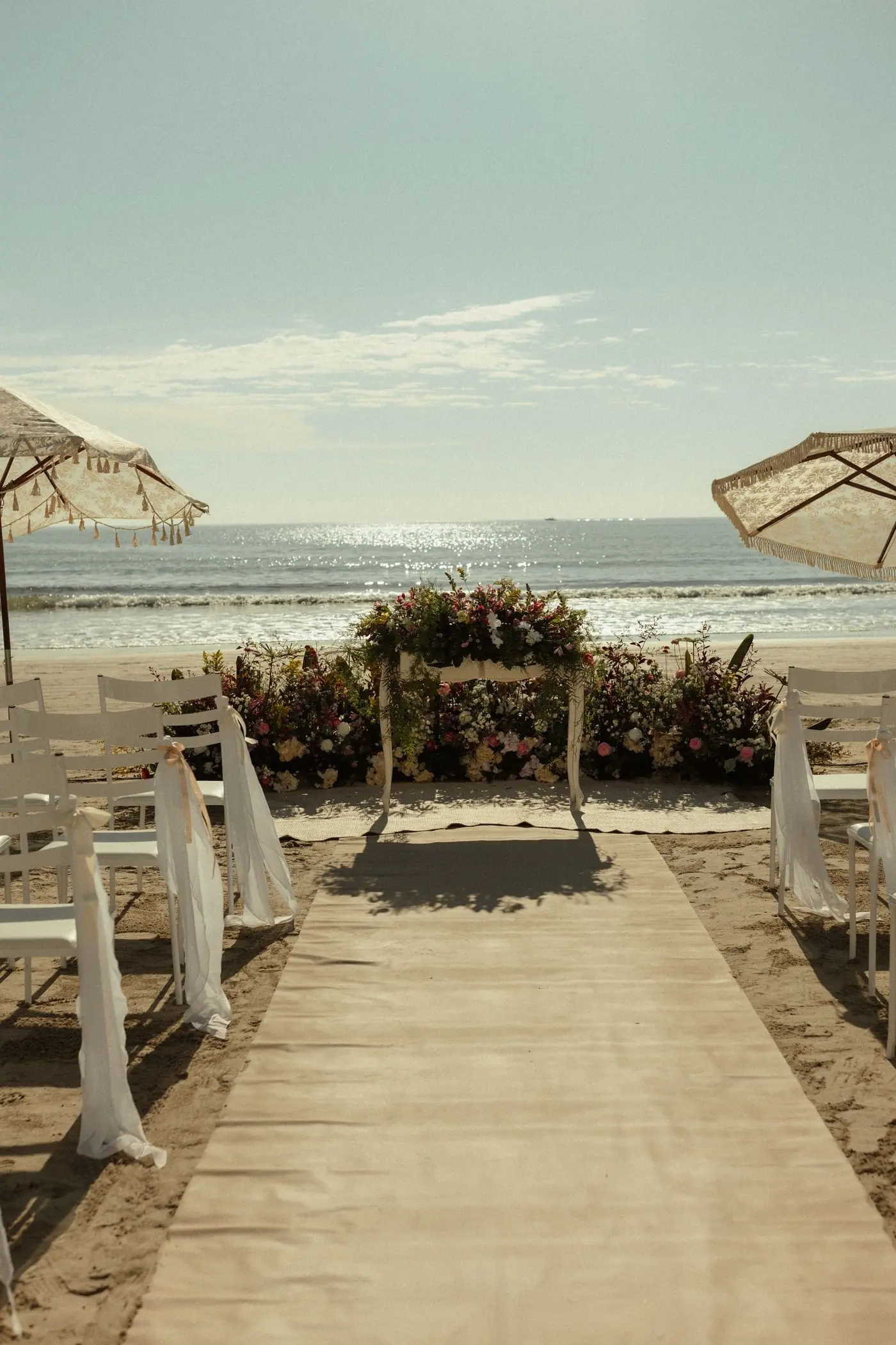 A ceremony set on the sand with parasols and a low floral table facing the sea