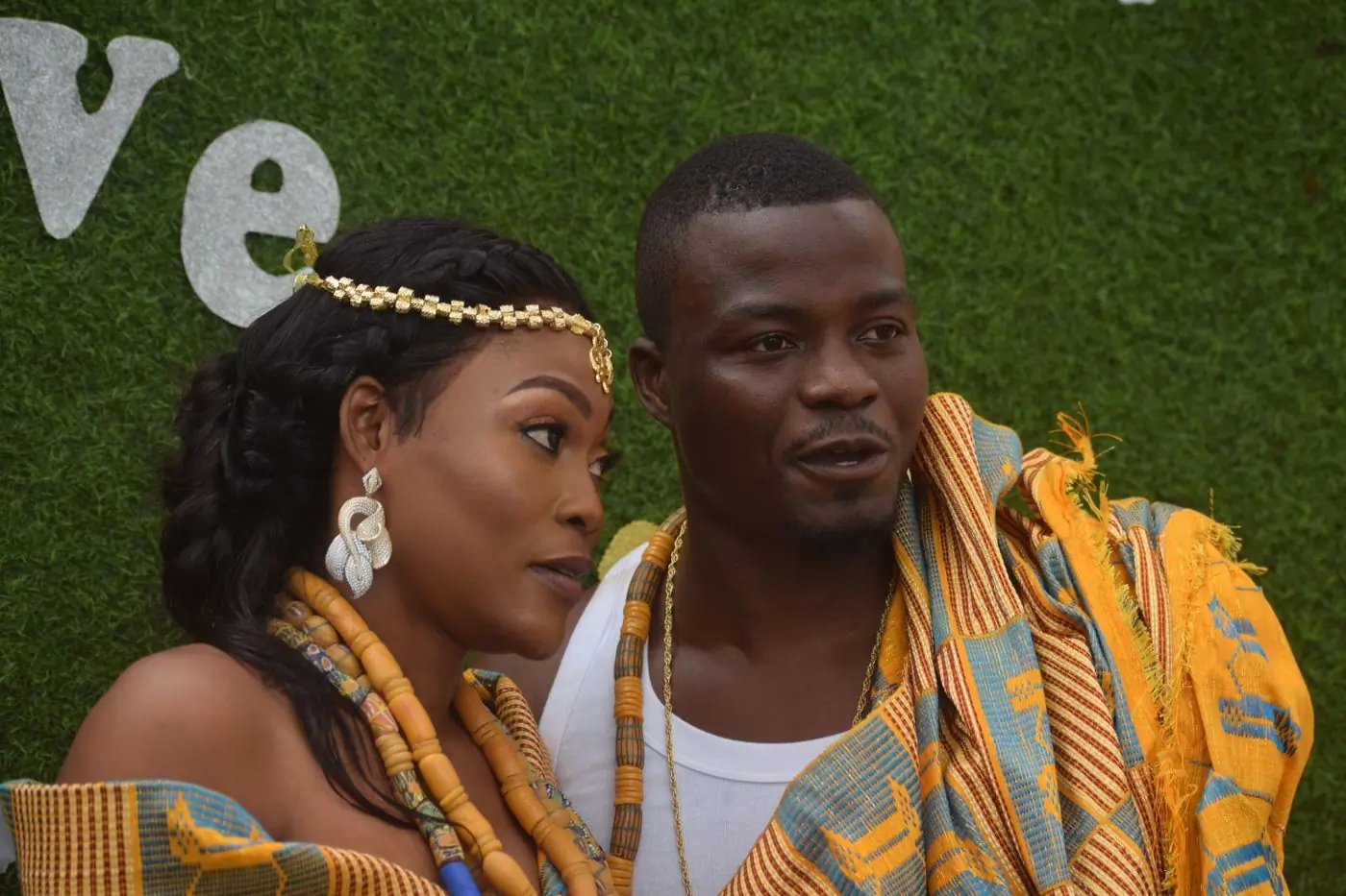 A couple in gold and kente cloth seated together at a traditional ceremony
