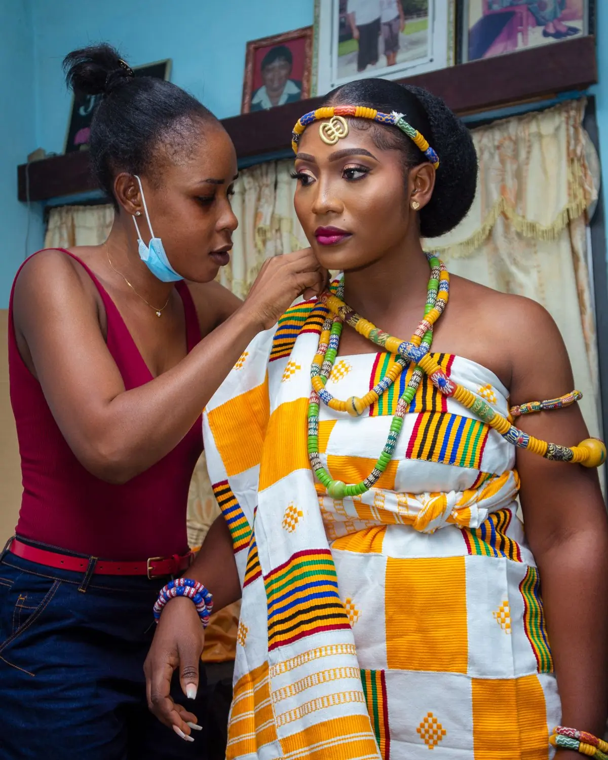 A bride being dressed in kente cloth and beads before a ceremony