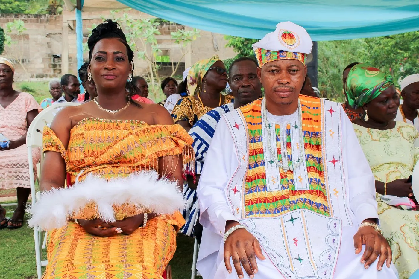 A couple in kente cloth seated together under a canopy at a traditional engagement