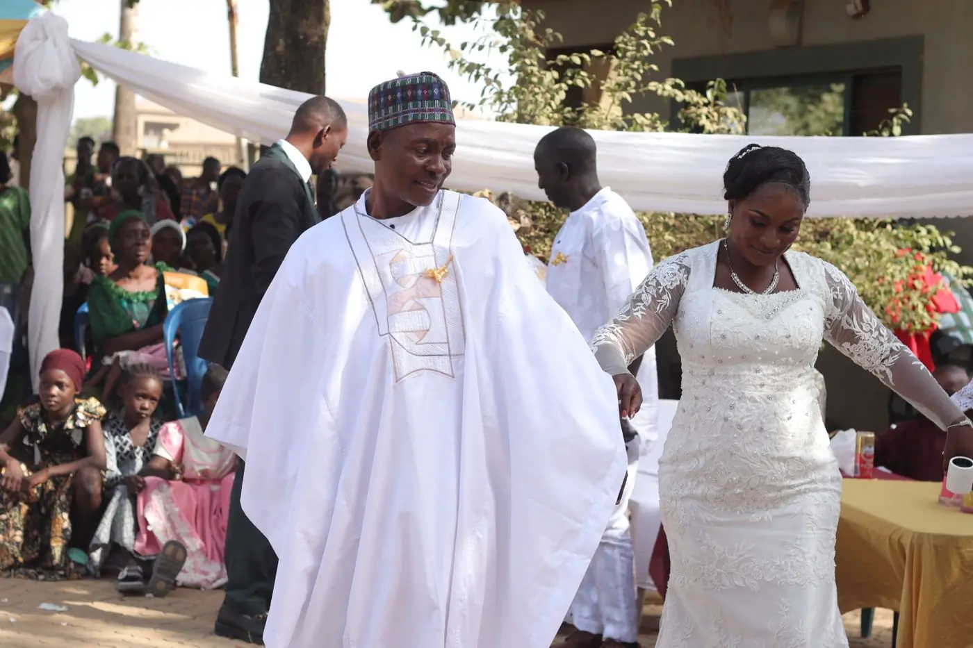 A bride and groom in white at an outdoor wedding ceremony