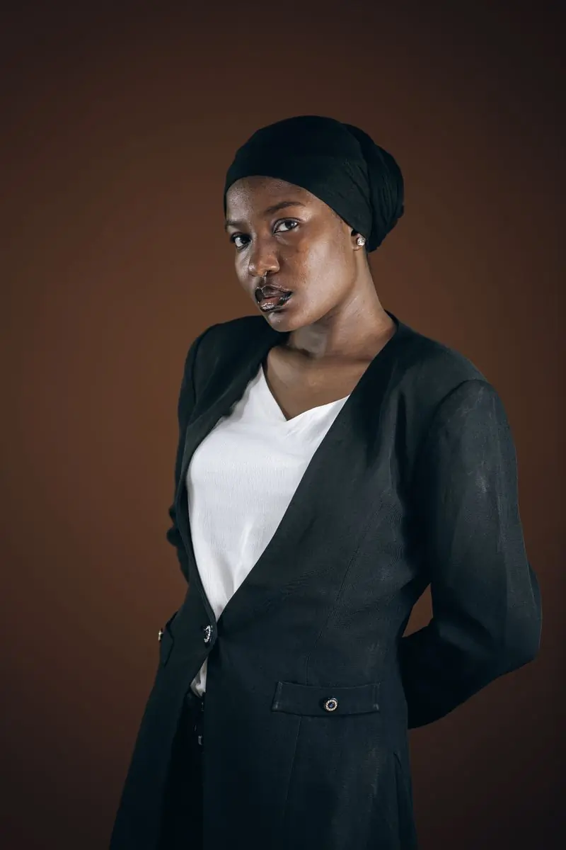 A woman in a black headwrap and jacket photographed against a warm backdrop