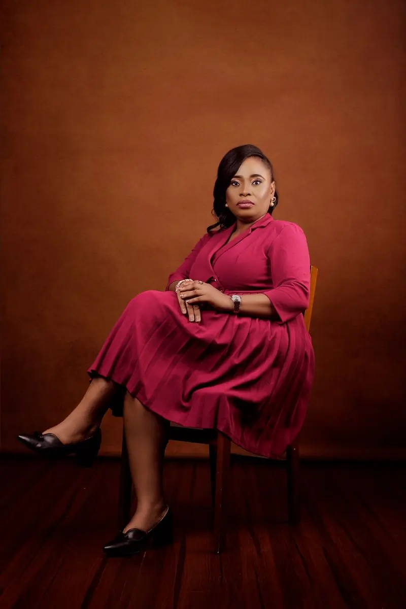 A woman seated in a deep pink dress photographed against a warm backdrop