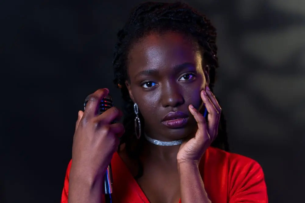 A close portrait of the artist with her hands raised to her face, lit deep red