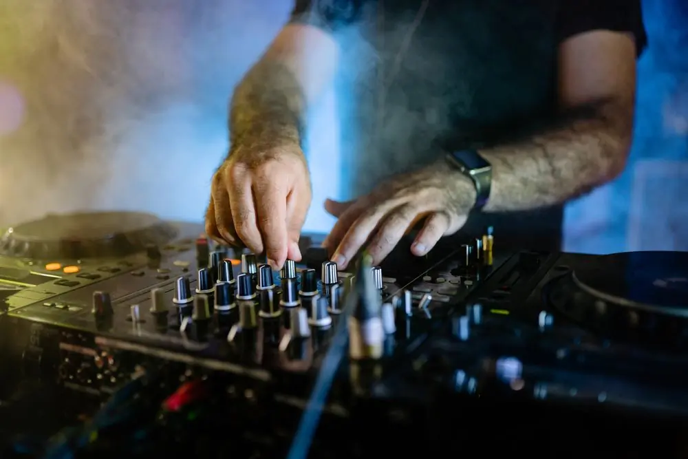 A pair of hands working an audio mixer under club lighting