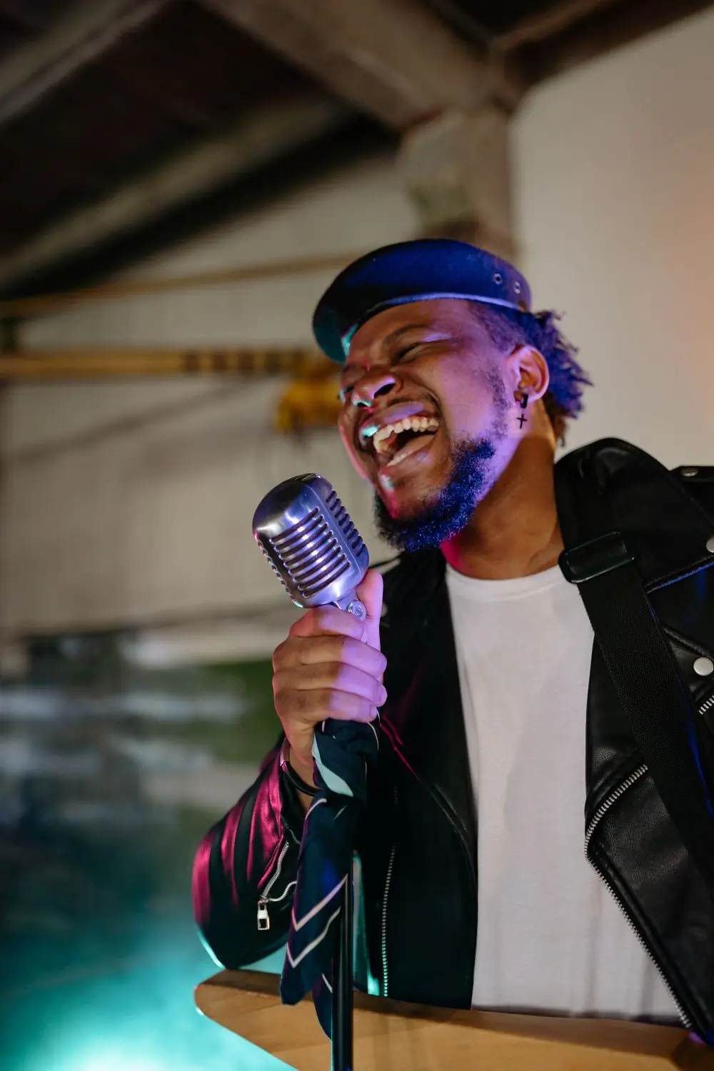 A vocalist singing into a chrome microphone under violet stage light