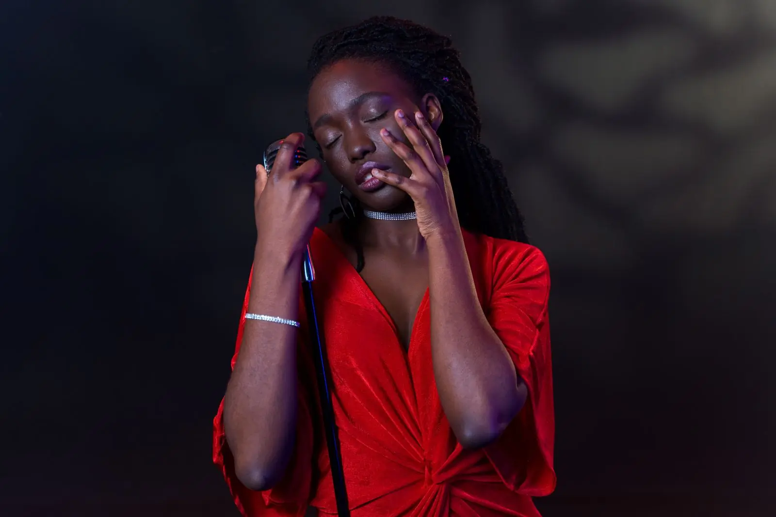 A vocalist with her eyes closed and her hands to her face, lit deep red