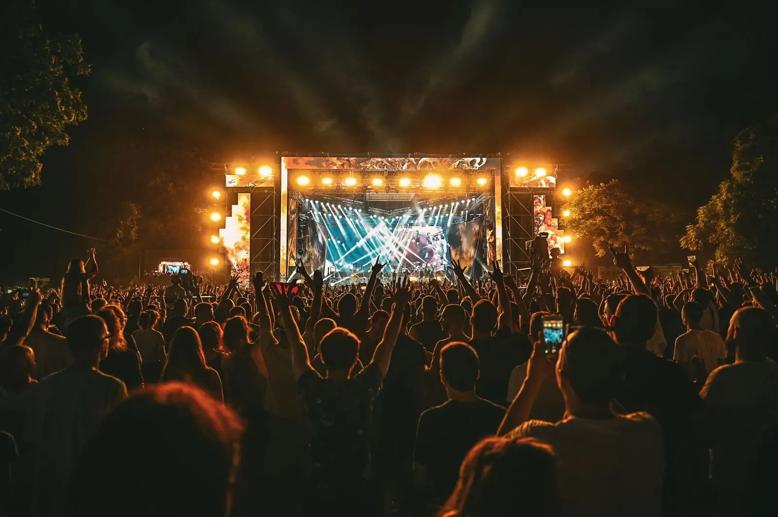An outdoor festival stage at night, lit warm above a large crowd