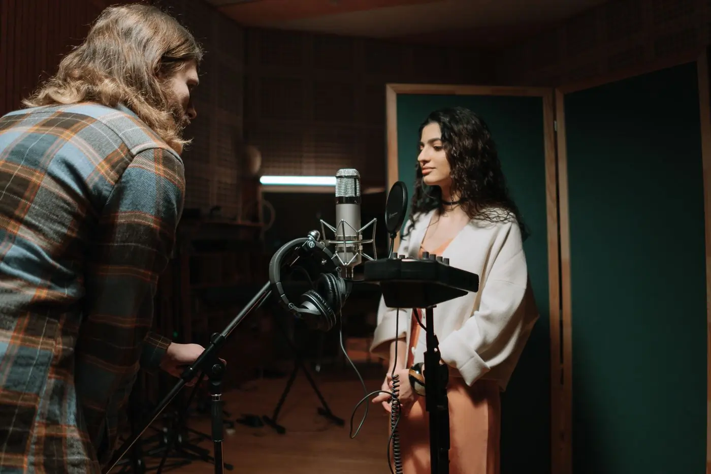 Two musicians recording a vocal take in a warmly lit studio